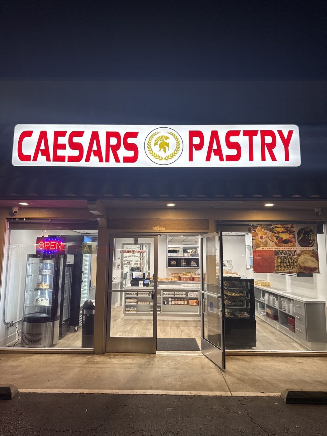 Caesar's Pastry storefront at night with the lit sign and open door